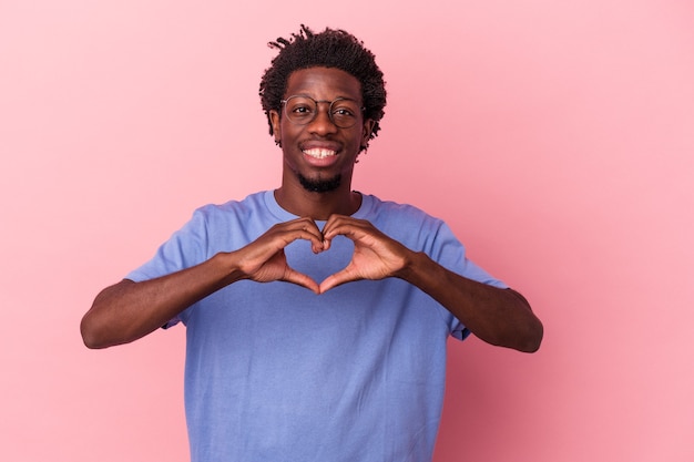 Giovane uomo afroamericano isolato su sfondo rosa sorridente e mostrando una forma di cuore con le mani.