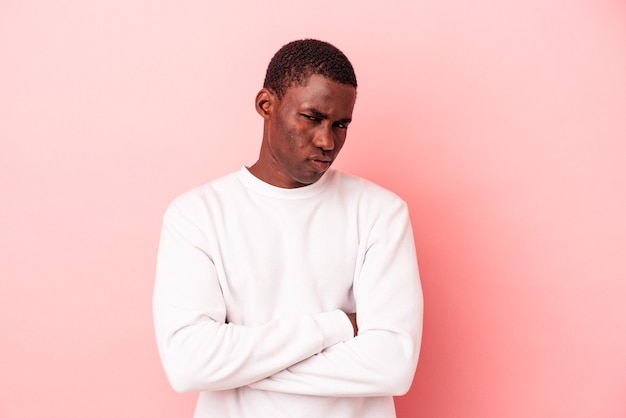 Giovane uomo afroamericano isolato su sfondo rosa sospettoso, incerto, esaminandoti.