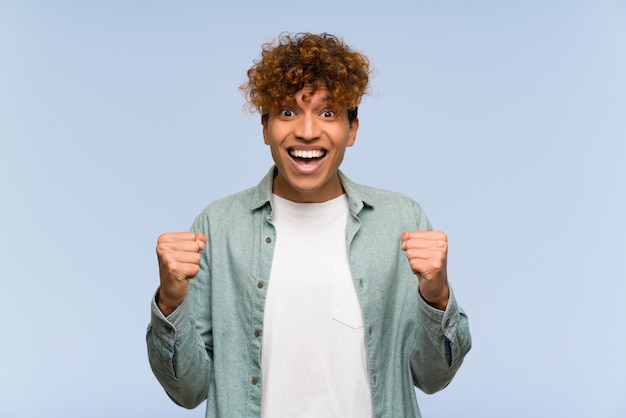 Giovane uomo afroamericano sopra isolato muro blu celebra una vittoria nella posizione del vincitore