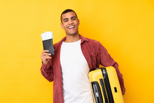 Giovane uomo afroamericano sopra la parete gialla isolata in vacanza con la valigia e il passaporto