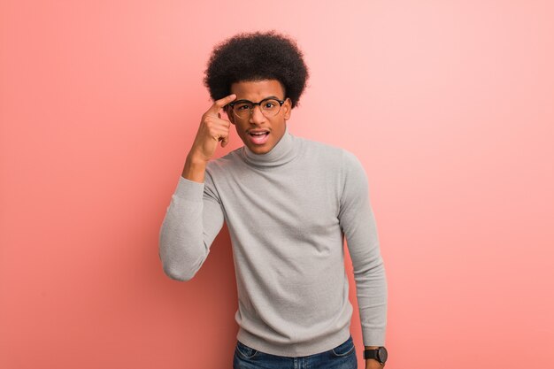 Giovane uomo afroamericano sopra una parete rosa che fa un gesto di delusione con il dito