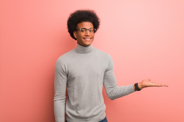 Giovane uomo afroamericano sopra una parete rosa che tiene qualcosa con la mano