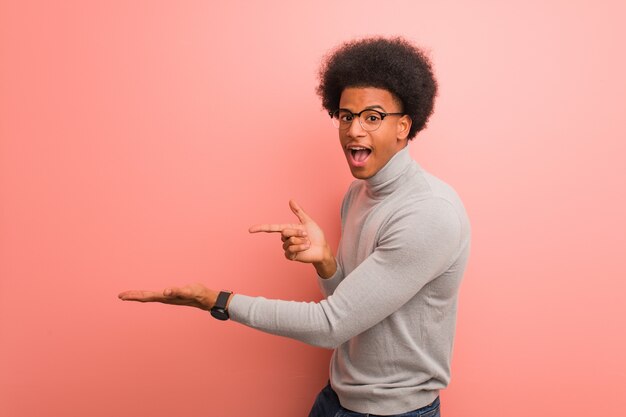 Giovane uomo afroamericano sopra una parete rosa che tiene qualcosa con la mano