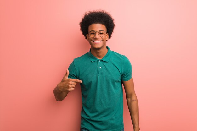 Giovane uomo afroamericano sopra una persona rosa della parete che indica a mano uno spazio della copia della camicia, fiero e sicuro