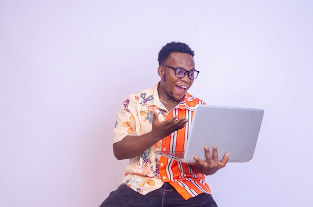 Giovane uomo afroamericano sorridente seduto e utilizzando il computer portatile isolato su sfondo bianco eccitato