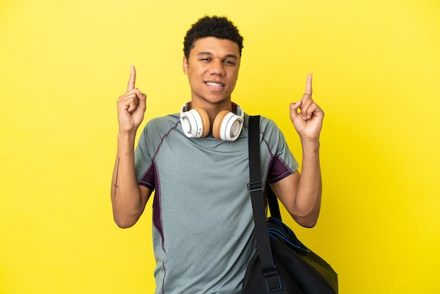 Giovane uomo afroamericano sportivo con borsa sportiva isolato su sfondo giallo che indica una grande idea