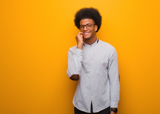 Giovane uomo afroamericano su un muro arancione mordere le unghie, nervoso e molto ansioso