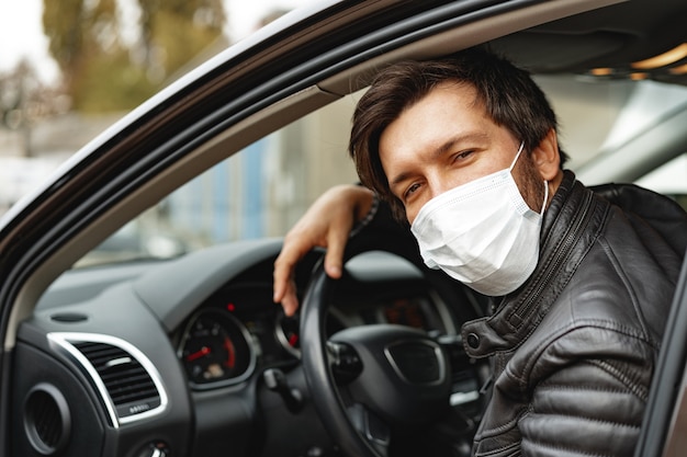 Giovane uomo alla guida di auto in mascherina medica