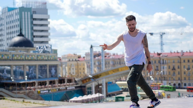 Giovane uomo alla moda che balla a stile libero sul cavalletto e canta il centro della città sullo sfondo