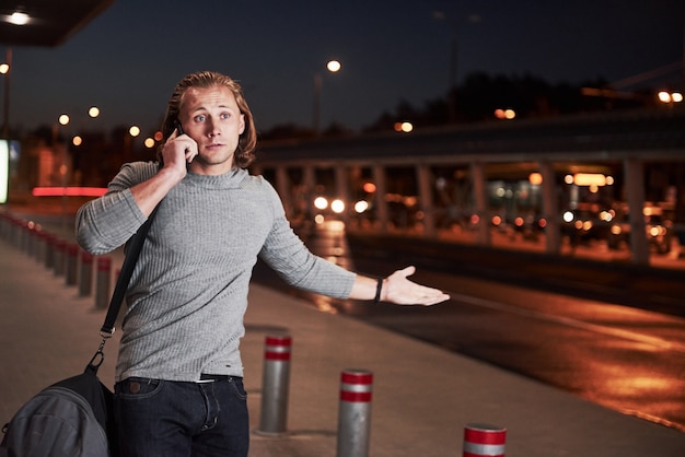 Giovane uomo alla moda che si muove nella notte vicino alla strada e parla al telefono having