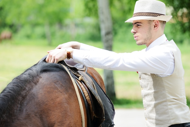 Giovane uomo alla moda tenendo a cavallo sulla campagna