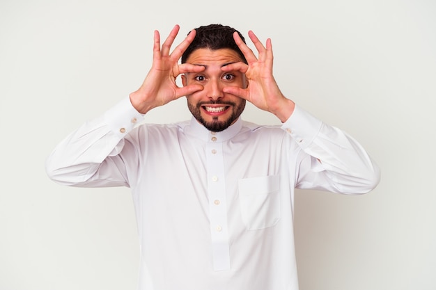 Giovane uomo arabo che indossa abiti tipici arabi isolati su sfondo bianco tenendo gli occhi aperti per trovare un'opportunità di successo.