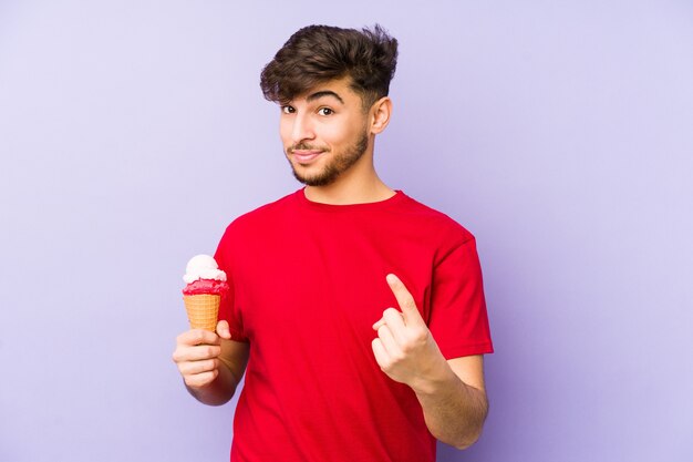 Giovane uomo arabo che tiene un gelato puntato contro di te come se invitando ad avvicinarsi.