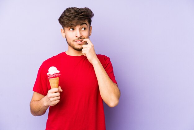 Giovane uomo arabo che tiene un gelato rilassato pensando a qualcosa guardando uno spazio di copia.