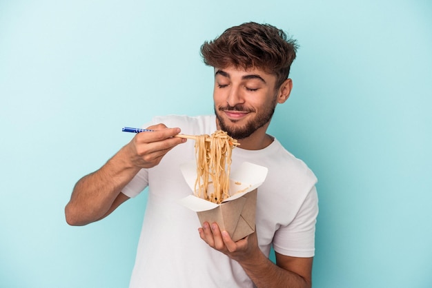 Giovane uomo arabo che tiene un noodles da asporto isolato su sfondo blu