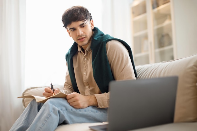 Giovane uomo arabo che utilizza il computer portatile seduto sul divano al coperto