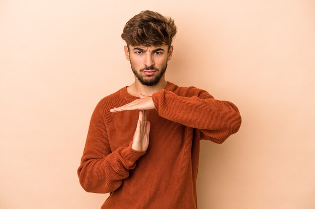 Giovane uomo arabo isolato su sfondo beige che mostra un gesto di timeout.