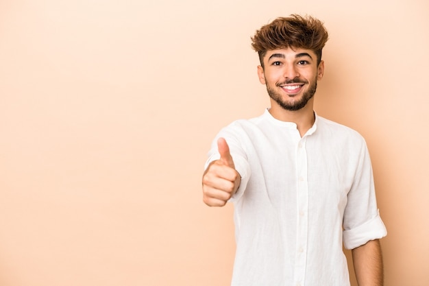 Giovane uomo arabo isolato su sfondo beige sorridente e alzando il pollice