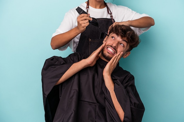 Giovane uomo arabo pronto a farsi tagliare i capelli isolato su sfondo blu