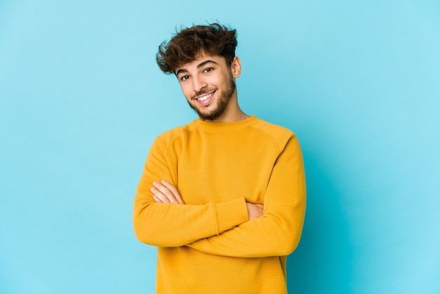 Giovane uomo arabo sulla parete blu che si sente fiducioso, incrociando le braccia con determinazione