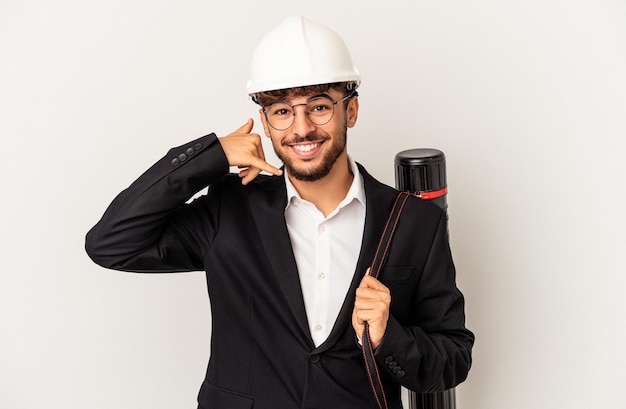 Giovane uomo architetto di razza mista che indossa un casco isolato su sfondo grigio che mostra un gesto di chiamata di telefonia mobile con le dita.