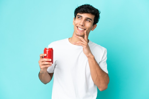 Giovane uomo argentino che tiene un rinfresco isolato su sfondo blu guardando in alto mentre sorride