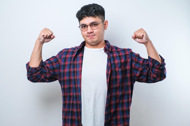 Giovane uomo asiatico bello che mostra i muscoli delle braccia sorridendo orgoglioso concetto di fitness
