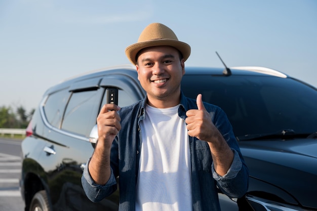 Giovane uomo asiatico bello che ottiene la nuova auto. Mostra la chiave dell'auto e molto felice. Acquista o noleggia un concetto di auto.