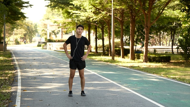 Giovane uomo asiatico bello fare jogging all'aperto ascoltando musica nel parco