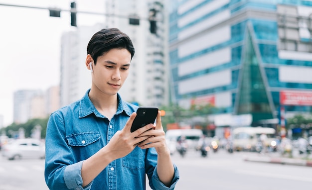 Giovane uomo asiatico che cammina e utilizza lo smartphone sulla strada