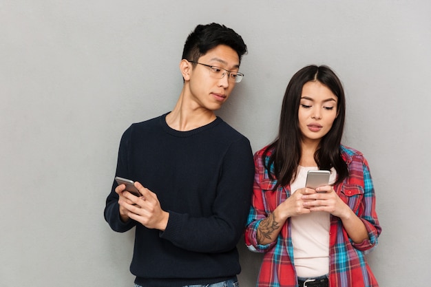 Giovane uomo asiatico che esamina la sua amica che chiacchiera dal telefono cellulare.