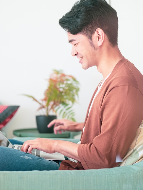 Giovane uomo asiatico che indossa abiti casual e usa il laptop