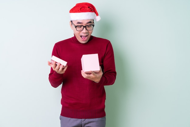 Giovane uomo asiatico che indossa il cappello di Natale su sfondo verde