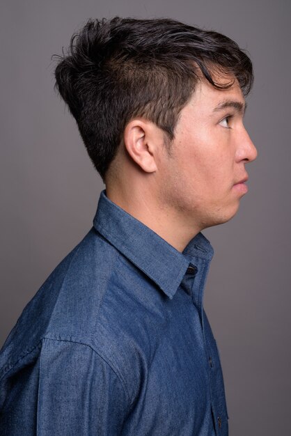 Giovane uomo asiatico che indossa la maglietta blu contro il muro grigio