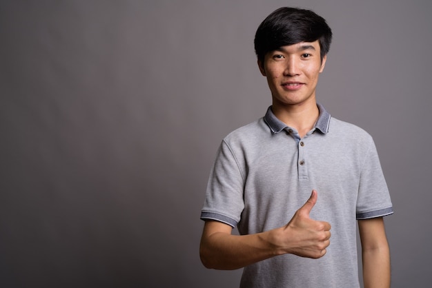 Giovane uomo asiatico che indossa la maglietta polo grigia contro il muro grigio