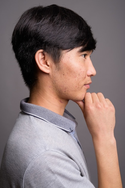Giovane uomo asiatico che indossa la maglietta polo grigia contro il muro grigio