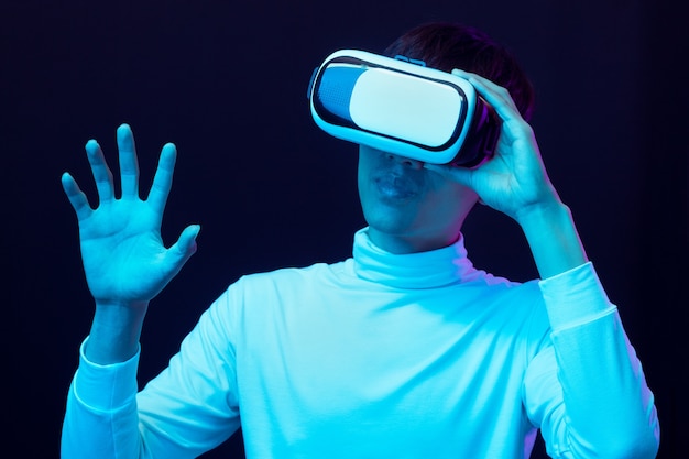Giovane uomo asiatico che indossa occhiali per realtà virtuale che guardano video a 360 gradi in luce al neon, concetto di tecnologia.