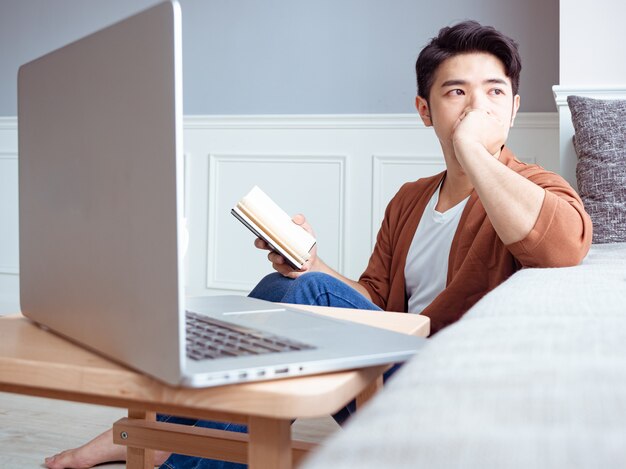 Giovane uomo asiatico che legge un libro mentre si rilassa a casa