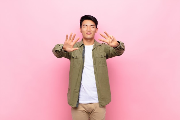 Giovane uomo asiatico che sorride e che sembra amichevole, mostrando numero otto o ottavo con la mano in avanti, conto alla rovescia sulla parete di colore