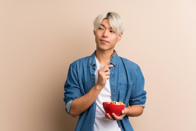 Giovane uomo asiatico che tiene una ciotola di cereali e di pensiero