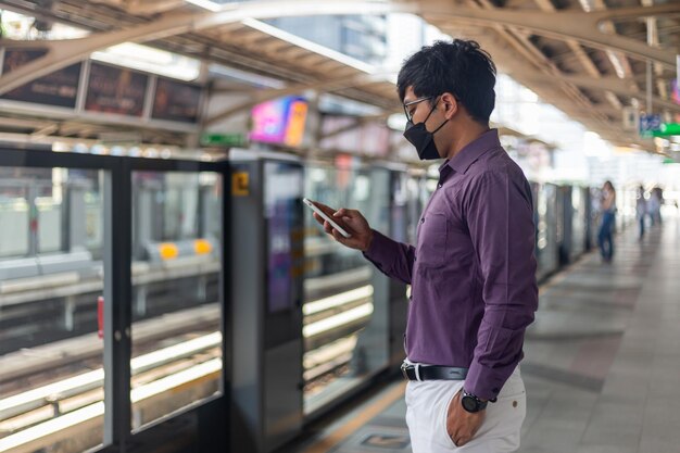 Giovane uomo asiatico che utilizza smartphone mentre aspetta la metropolitana o lo sky train.