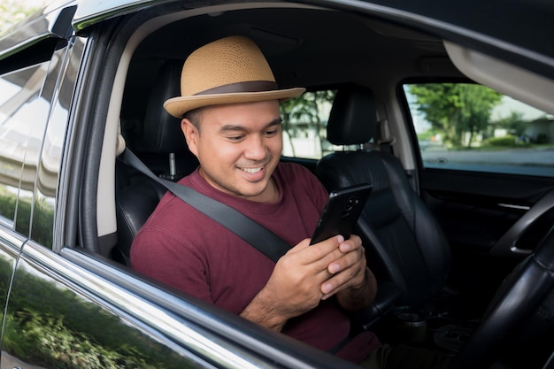 Giovane uomo asiatico che utilizza smartphone mentre guida l'auto.