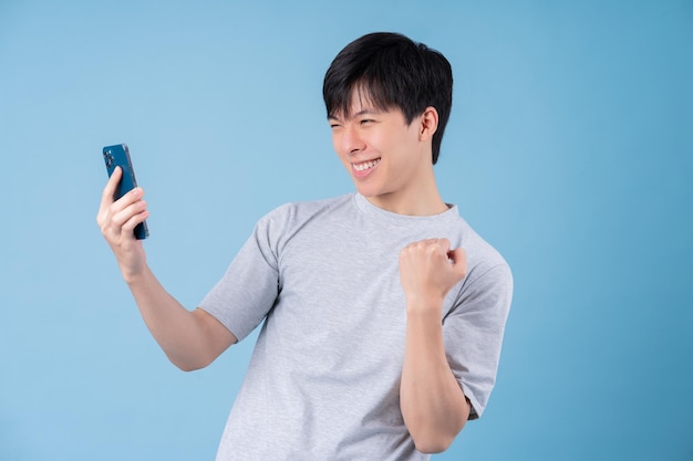 Giovane uomo asiatico che utilizza smartphone su sfondo blu