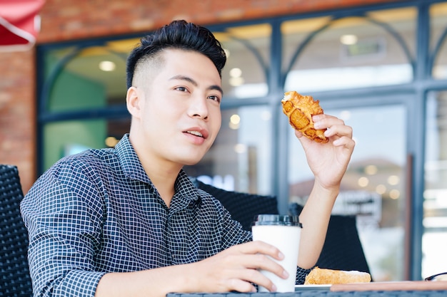 Giovane uomo asiatico con cooffee e pasticceria