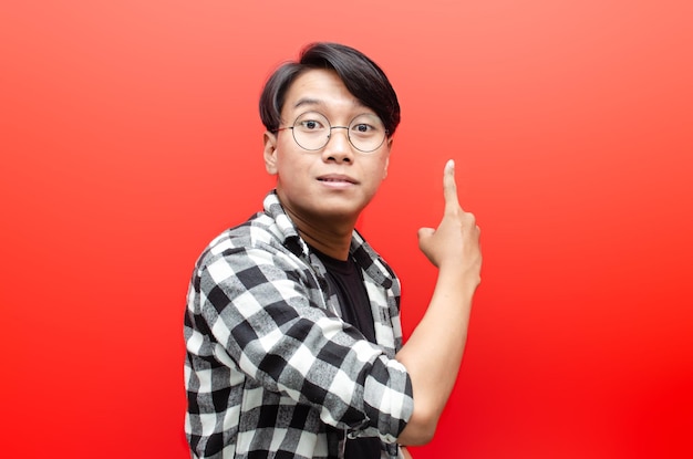 giovane uomo asiatico con un sorriso che indica offerte e presenta un annuncio pubblicitario isolato su rosso.