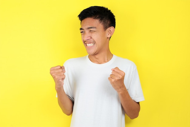 Giovane uomo asiatico felice ed emozionato che esprime gesto vincente. Successo e celebrazione su sfondo giallo