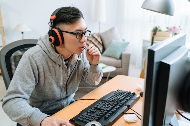 giovane uomo asiatico in cuffia con computer pc che gioca a casa. ragazzo cinese fanatico della dipendenza dalla tecnologia con giochi online con un amico e parlando con il microfono delle cuffie con il compagno di squadra su internet