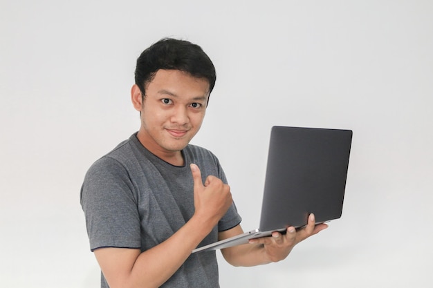 Giovane uomo asiatico in maglietta grigia Sentendosi felice e sorridere con il laptop in mano