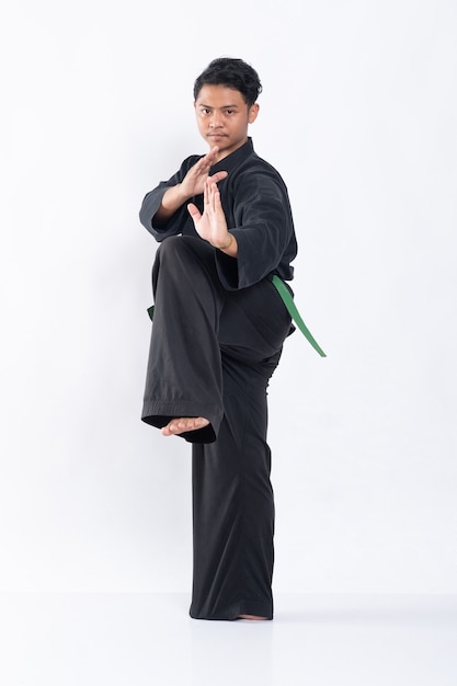 Giovane uomo asiatico in uniforme pencak silat con un piede sollevato con entrambe le mani pronte