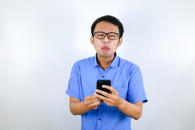 Giovane uomo asiatico piangere e triste quando guarda e usa il telefono Indonesia Uomo indossa occhiali e camicia blu Sfondo blu isolato